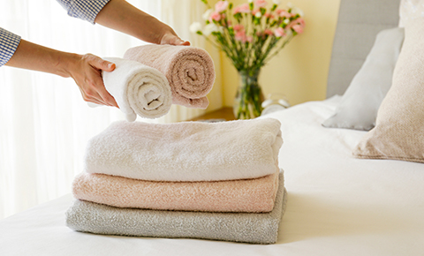a person placing clean grey, pink and white towels on a freshly made bed in a bed and breakfast